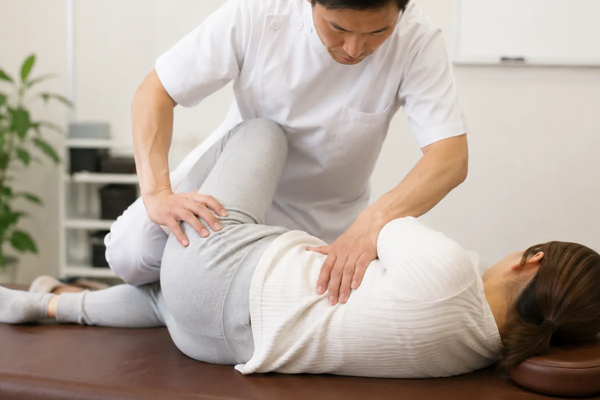 骨盤矯正の施術イメージ。あお向けの女性の骨盤まわりを施術者が手で調整しているところ